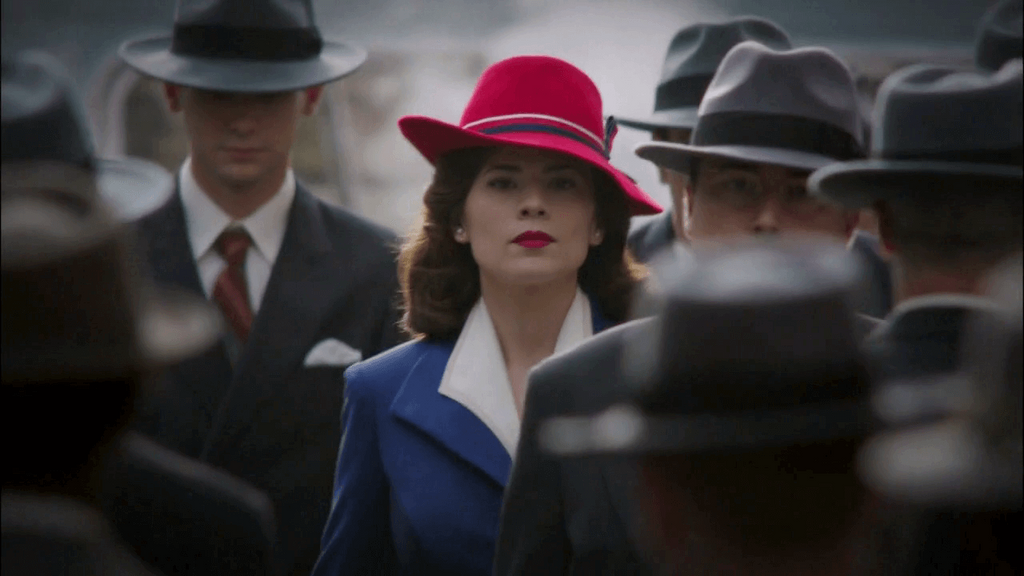 woman in bright red hat blue jacket amidst a black and white crowd