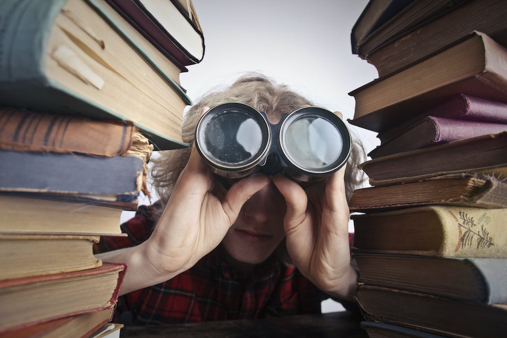 person looking through binoculars through two stacks of books